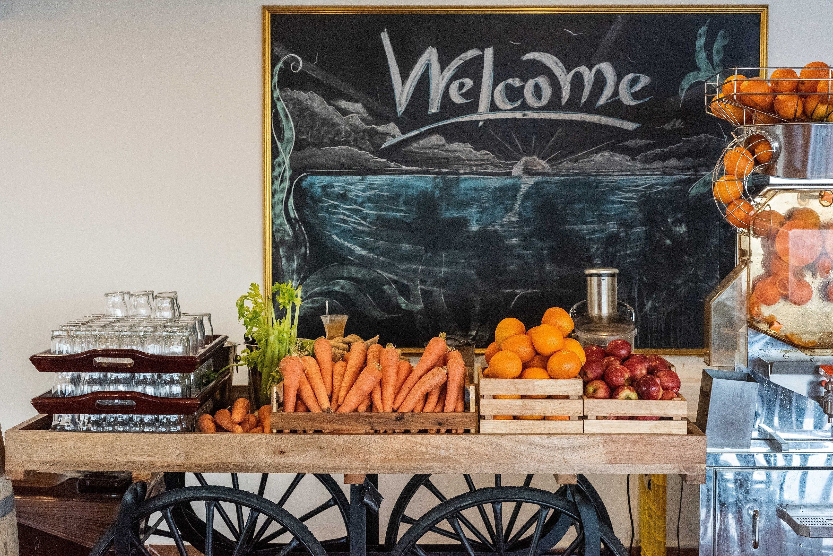 A welcome sign with a scenic background, a fruit and vegetable display, and a beverage dispenser.