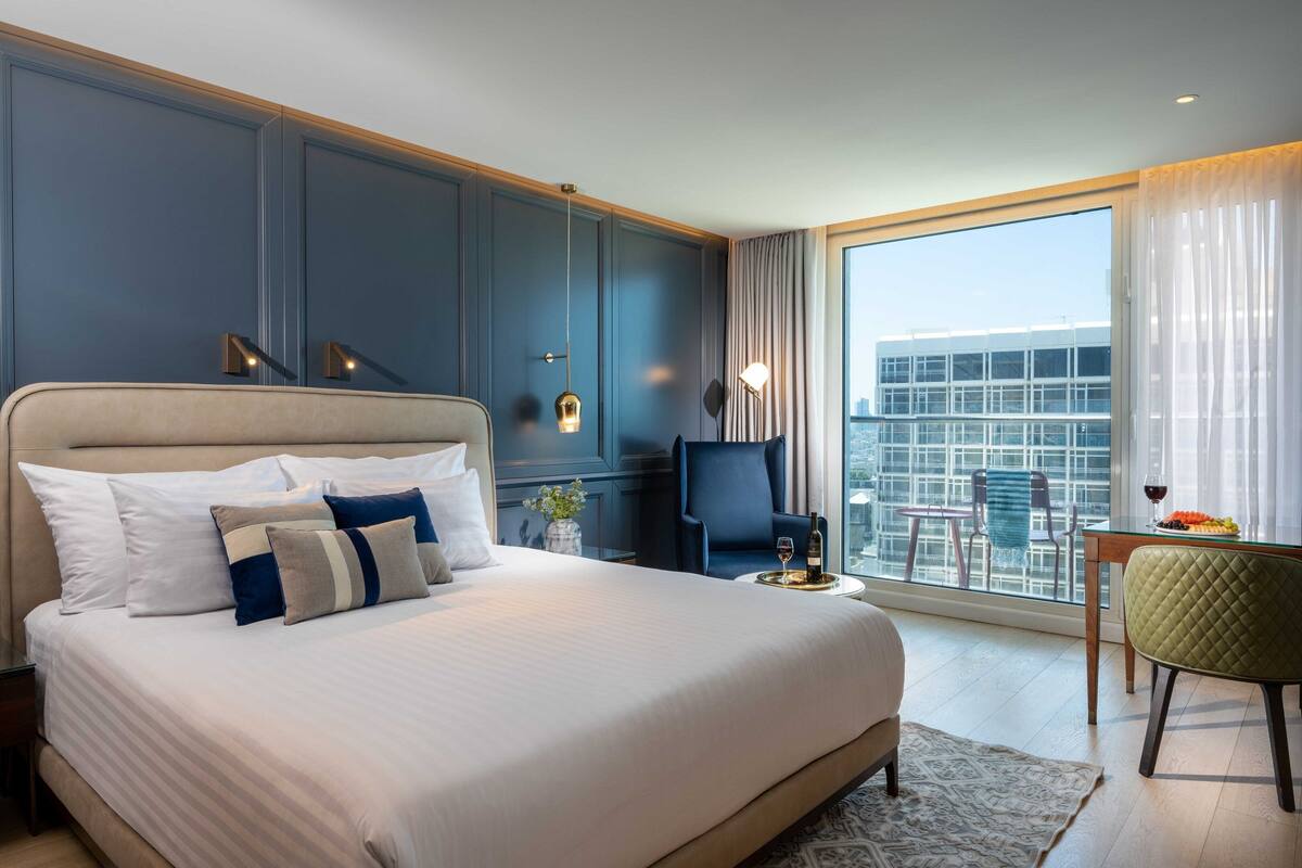 Une chambre d’hôtel dotée d’un grand lit, offrant une vue sur la ville, comprenant un coin repas et un balcon avec une table et des chaises.
