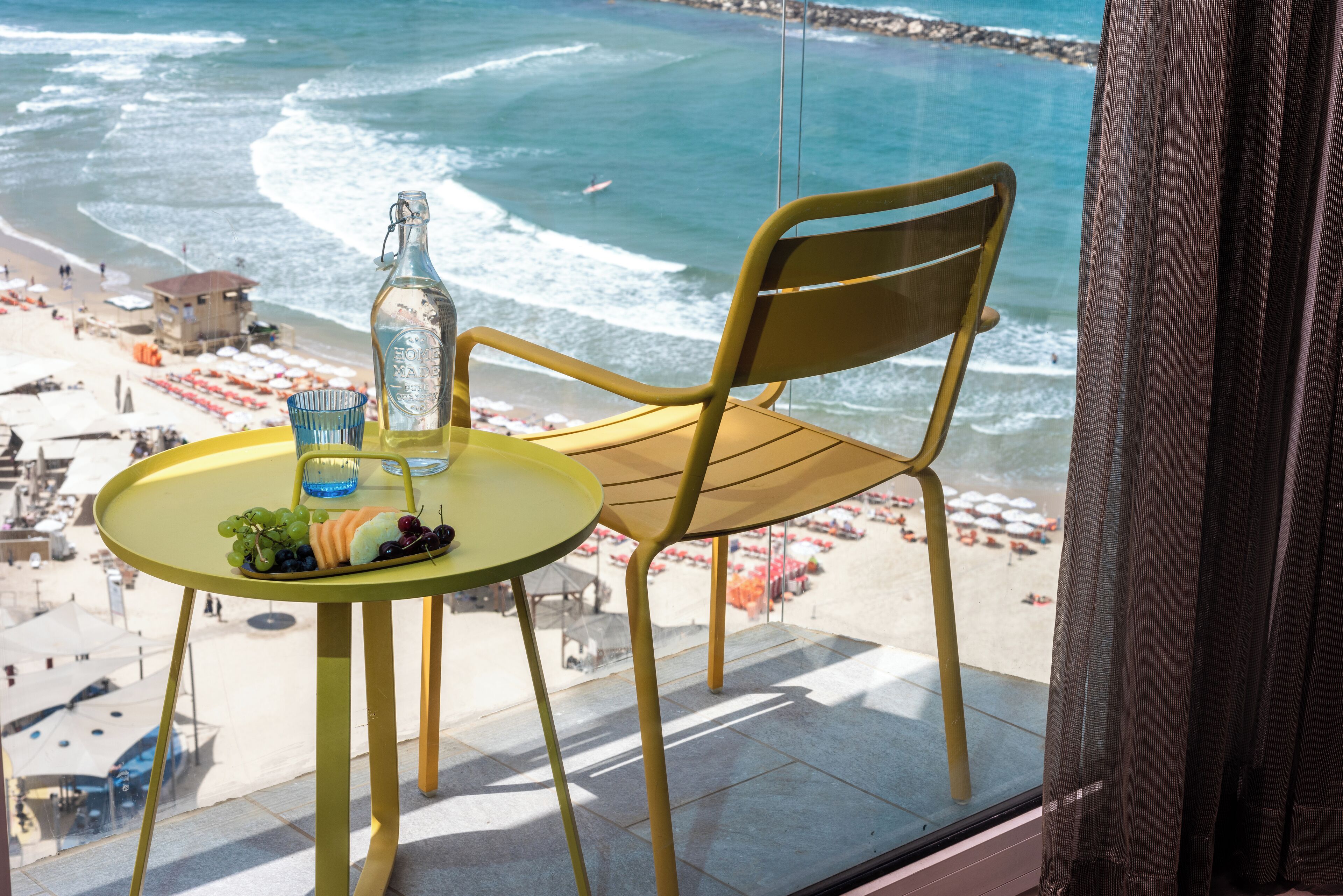Une table avec une bouteille et un verre, une chaise, et une vue sur la plage et l’océan.