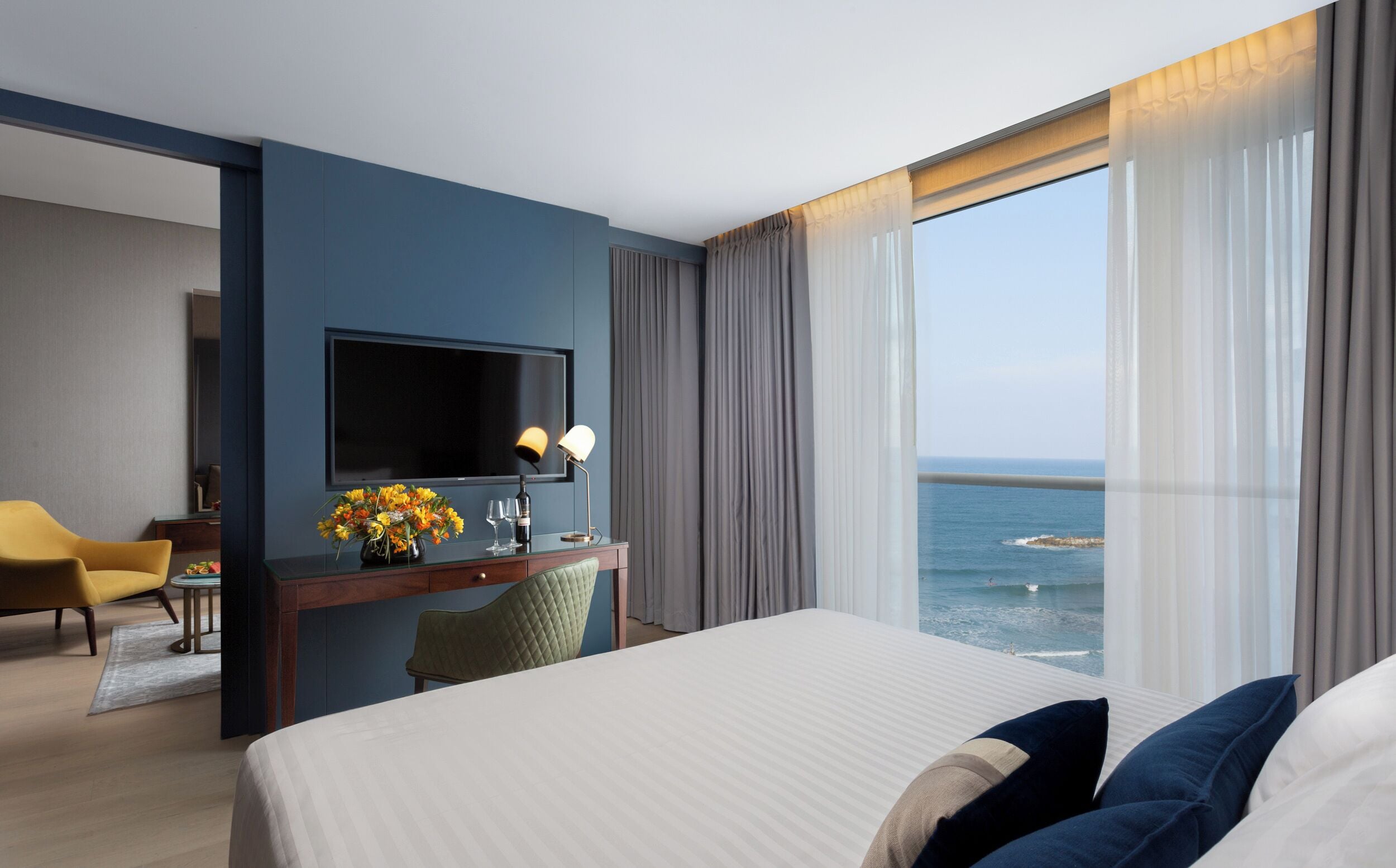 Ein Hotelzimmer mit einem großen Bett, einem Schreibtisch, einem Flachbildfernseher, einem Sessel und Blick aufs Meer.