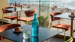A table with a dessert, a glass of water, and a blue bottle, overlooking a beach with people and a pier. - Crowne Plaza Tel Aviv Beach by IHG (Tel Aviv)