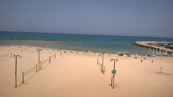 A beach with a volleyball net, a rocky breakwater, and sailboats.
