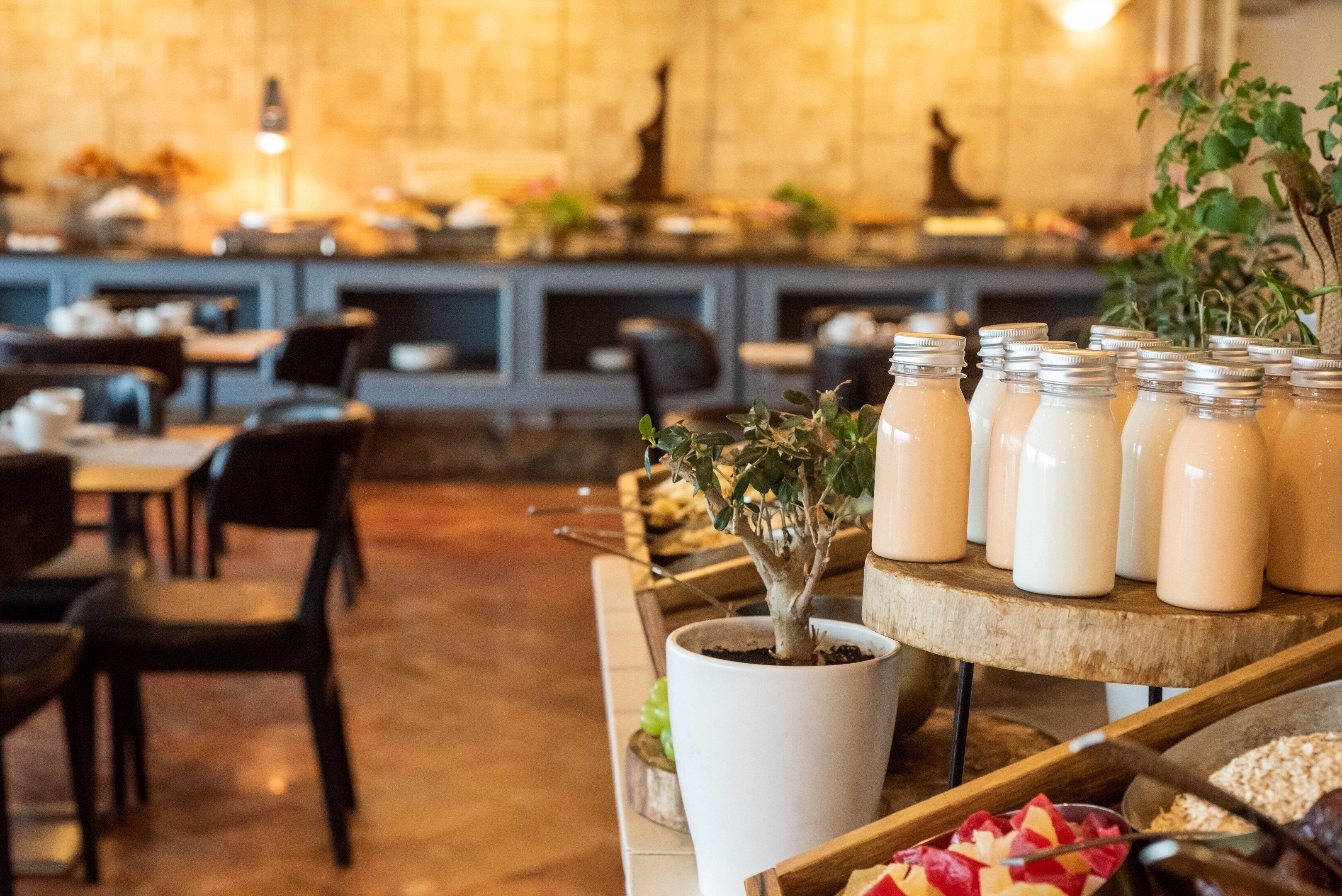 Een restaurantinterieur met een lange toonbank waarop eten en drinken staan, houten stoelen en een potplant.