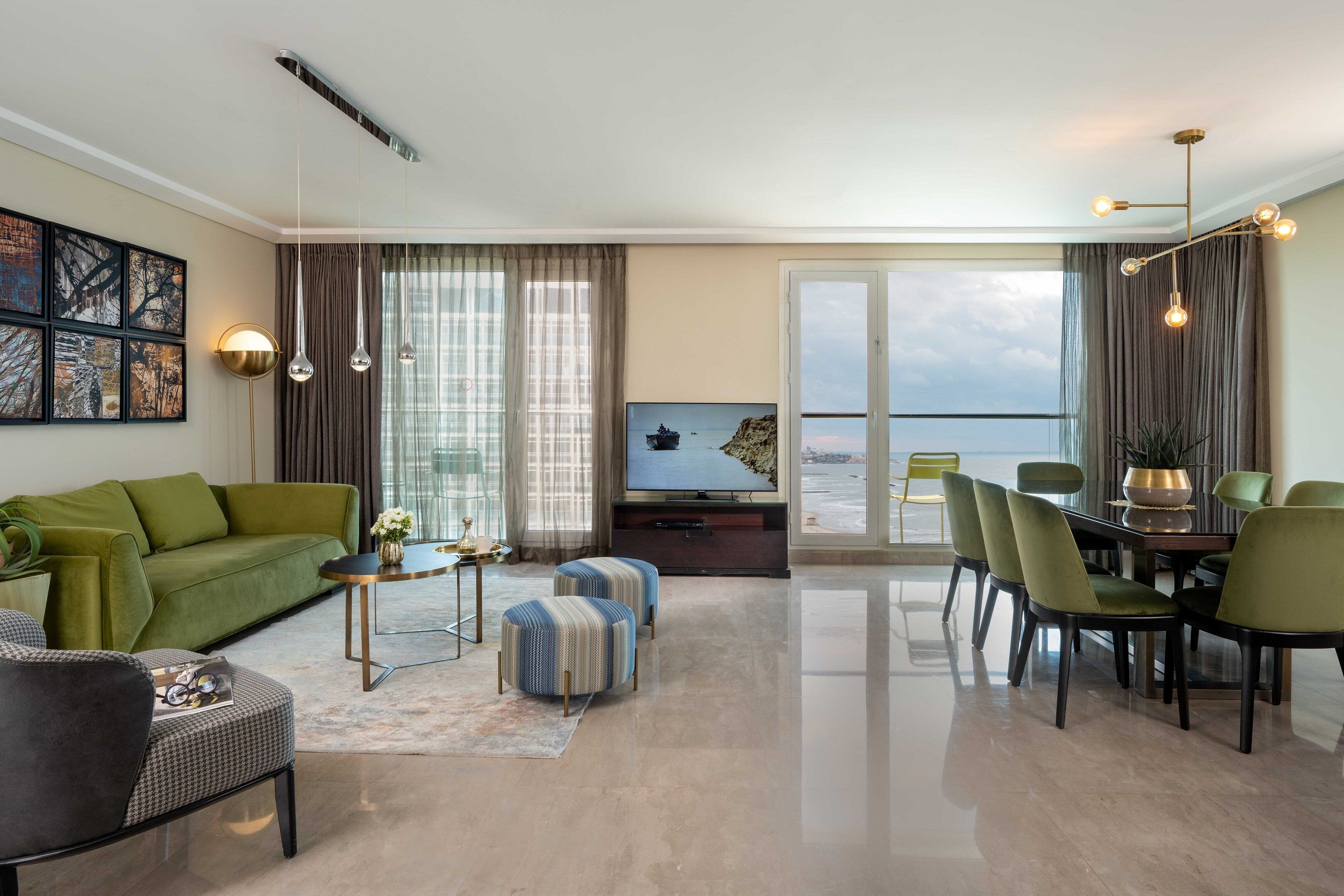 Uma sala de estar moderna com um sofá verde, uma mesa de centro redonda, uma televisão e uma varanda com vista para o mar.