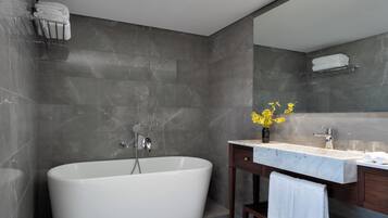 A modern bathroom with a freestanding bathtub, a vanity with a mirror, and a vase of yellow flowers.