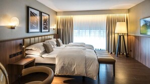 A hotel room with a large bed, a bedside table, a chair, a floor lamp, and a view of the outdoors through the window. - Central Plaza Hotel (Zürich)