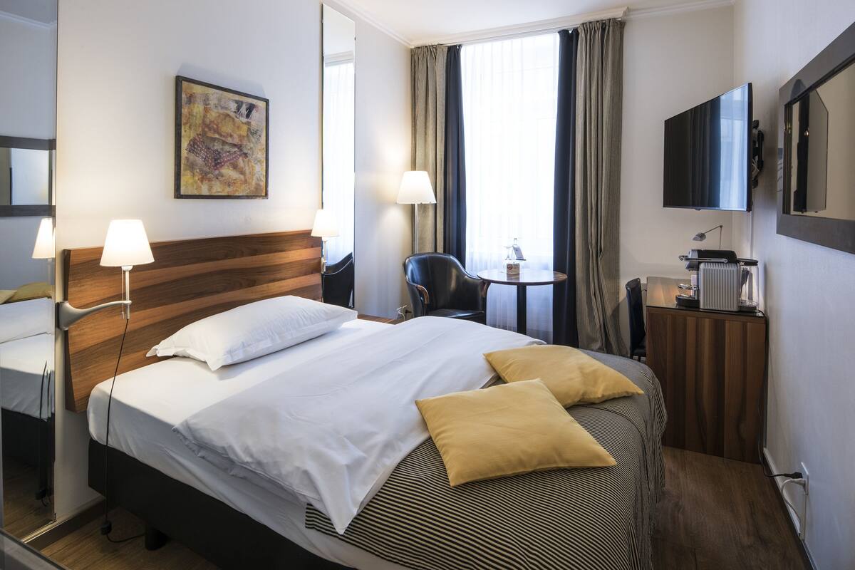 A hotel room with a large bed, a desk, a chair, a television, and a window with curtains.