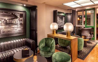 A modern lounge area with a leather sofa, green velvet chairs, and a wooden side table with two lamps.