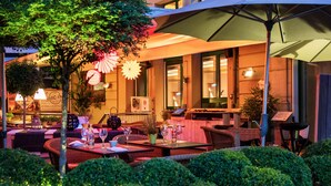 An outdoor dining area with wicker furniture, tables, and chairs, surrounded by well-maintained bushes. - Central Plaza Hotel (Zürich)