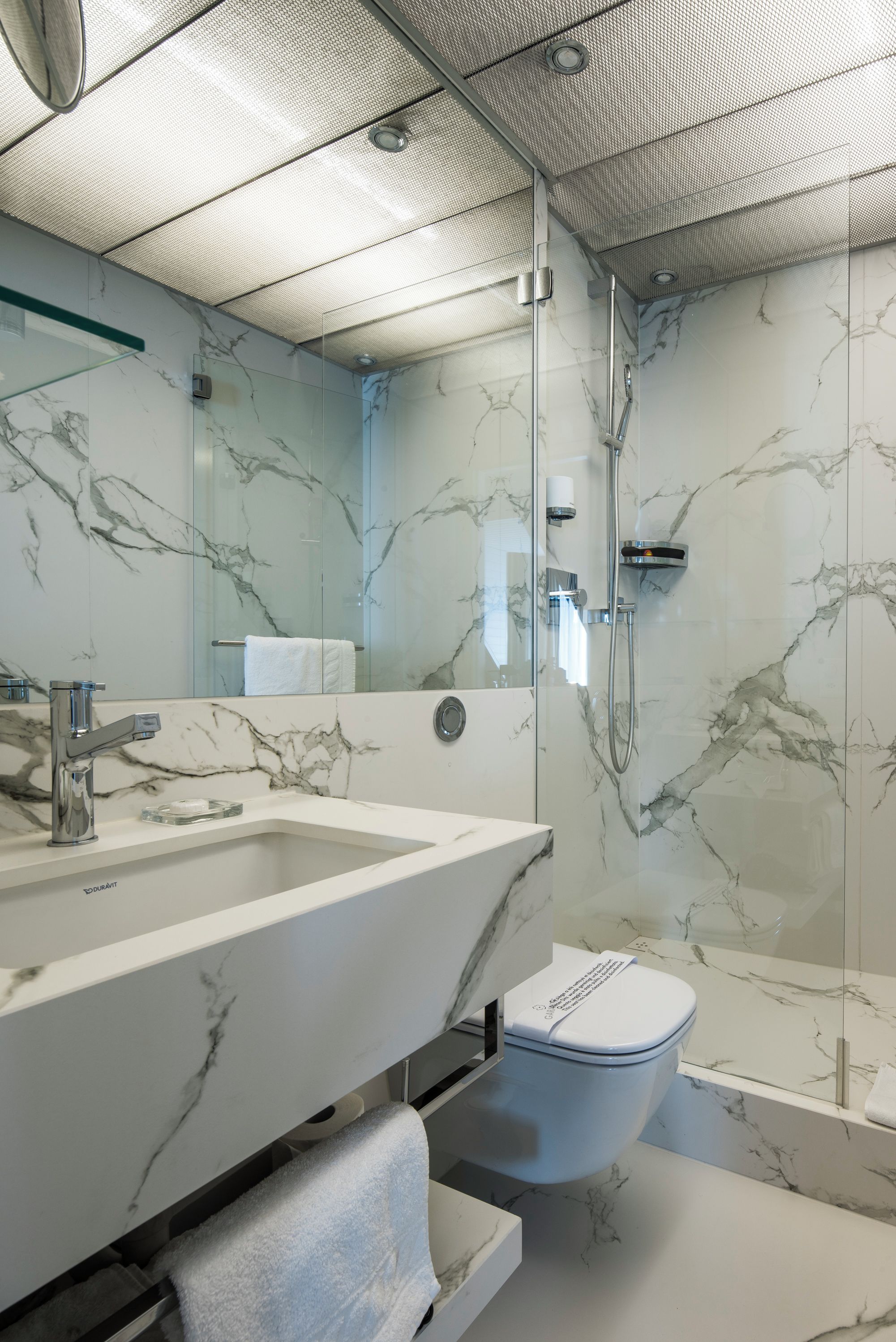 Un baño moderno con ducha de vidrio, lavamanos de mármol y un inodoro.