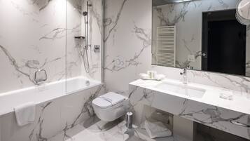 Un baño moderno con pared de mármol, una bañera, un inodoro y un lavamanos con espejo.