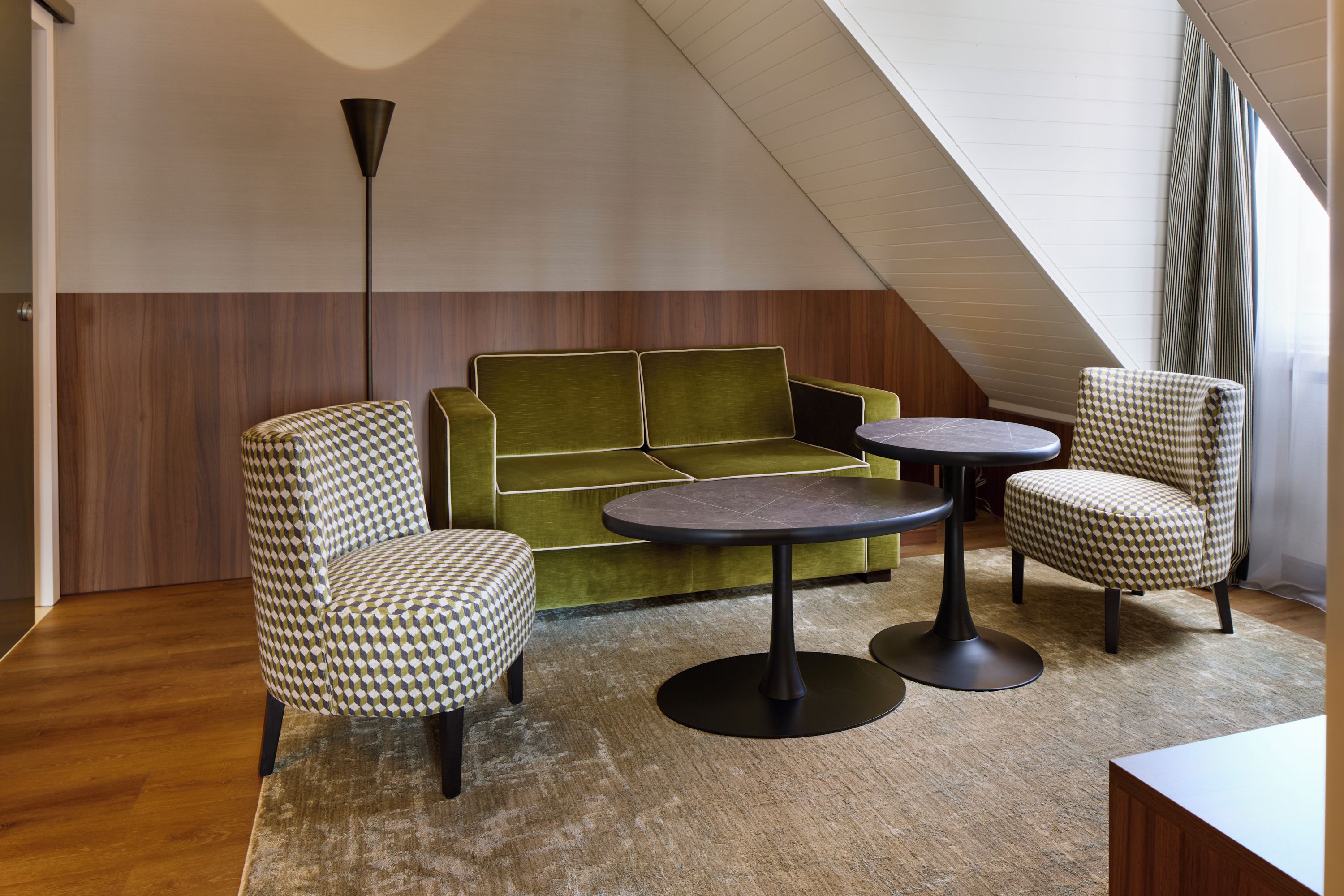 A modern interior with a green sofa, patterned armchairs, and a round table.