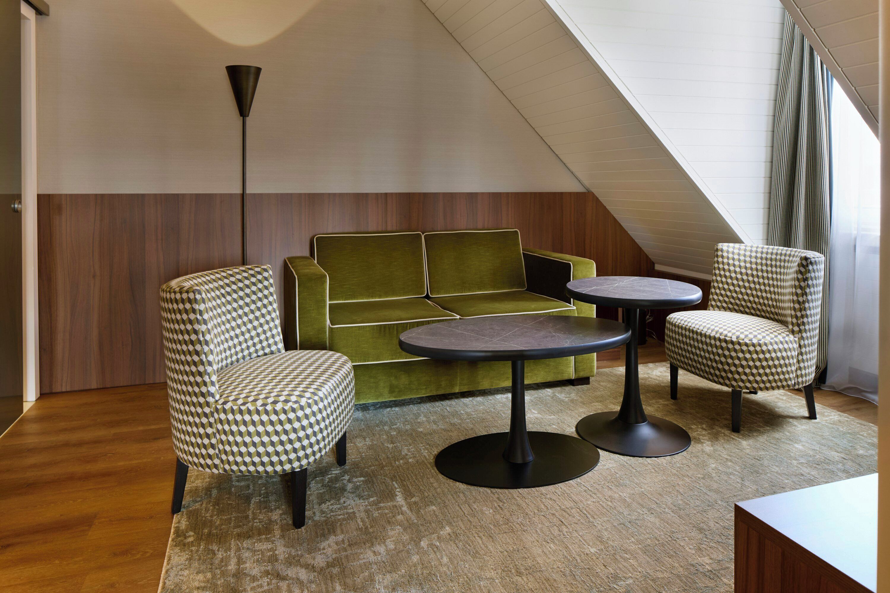A modern interior with a green sofa, patterned armchairs, and a round table.