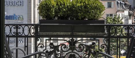 Un balcón con mesa y sillas, con vista a un paisaje urbano que incluye edificios y la aguja de una iglesia.