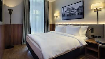 A hotel room with a large bed, a bedside table, a round table, a wall-mounted lamp, and a framed picture.