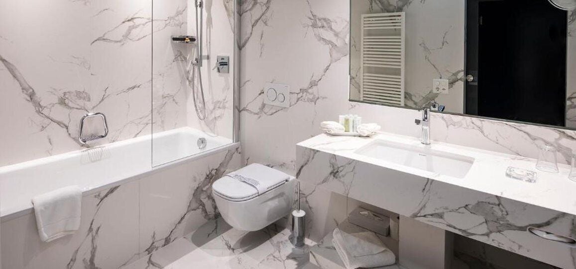 A modern bathroom with a marble wall, a bathtub, a toilet, and a sink.