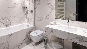 A modern bathroom with a marble wall, a bathtub, a toilet, and a sink.