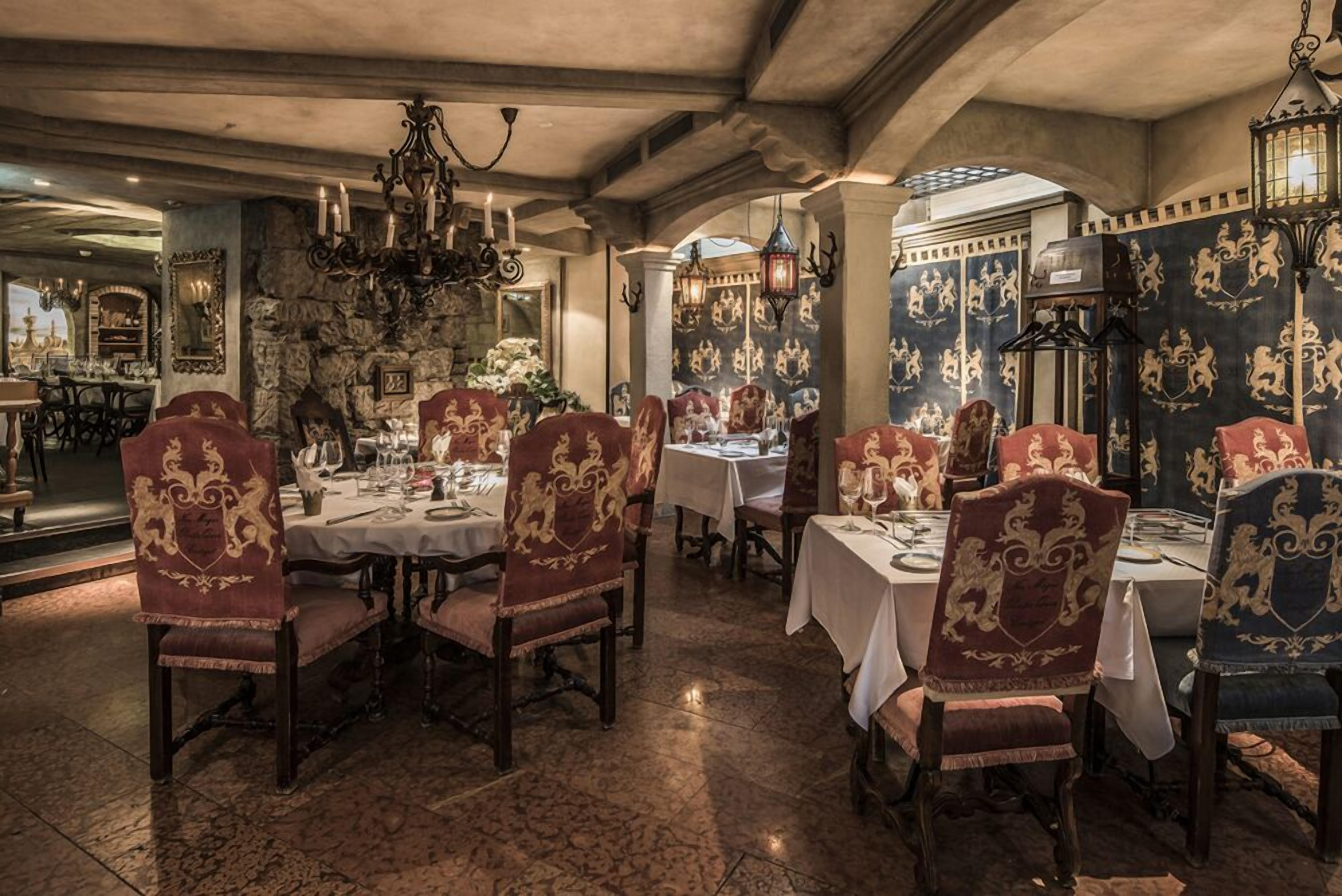 A dining area with ornate chairs, chandeliers, and patterned wallpaper.