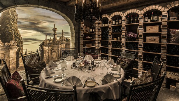A dining area with a round table set for four, surrounded by ornate chairs, and a wine rack with bottles behind the table. - Central Plaza Hotel (Zürich)
