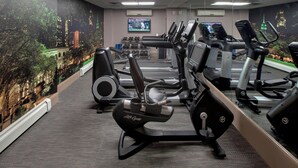 A gym with various exercise equipment, a digital clock displaying "THU JUL 06", and a cityscape mural on the wall.