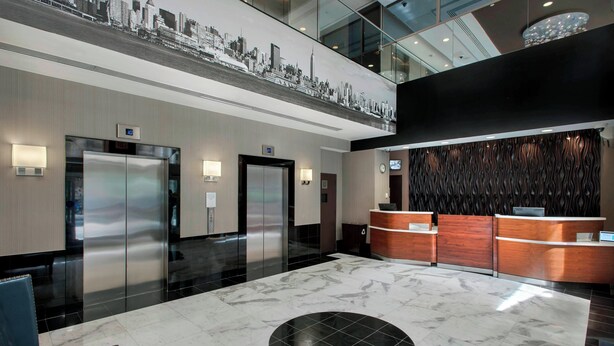 A modern hotel lobby with a marble floor, two elevators, a reception desk, and a cityscape mural on the ceiling.