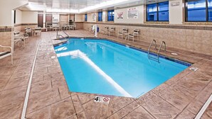 An indoor swimming pool with clear water, tiled walls, and a tiled floor. There are lounge chairs and a changing room in the background. - AmericInn by Wyndham Omaha (Omaha)