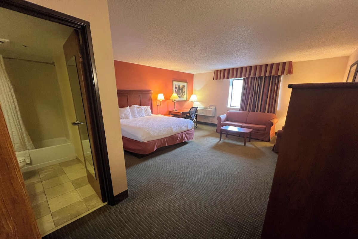 Ein Hotelzimmer mit Bett, Schreibtisch, Stuhl, einer Couch und einem Badezimmer mit Dusche und Toilette.