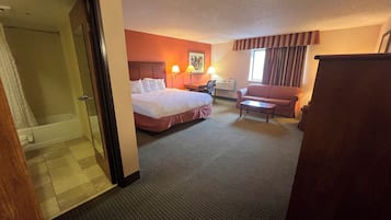 A hotel room with a bed, a desk, a chair, a sofa, and a bathroom with a shower and toilet.