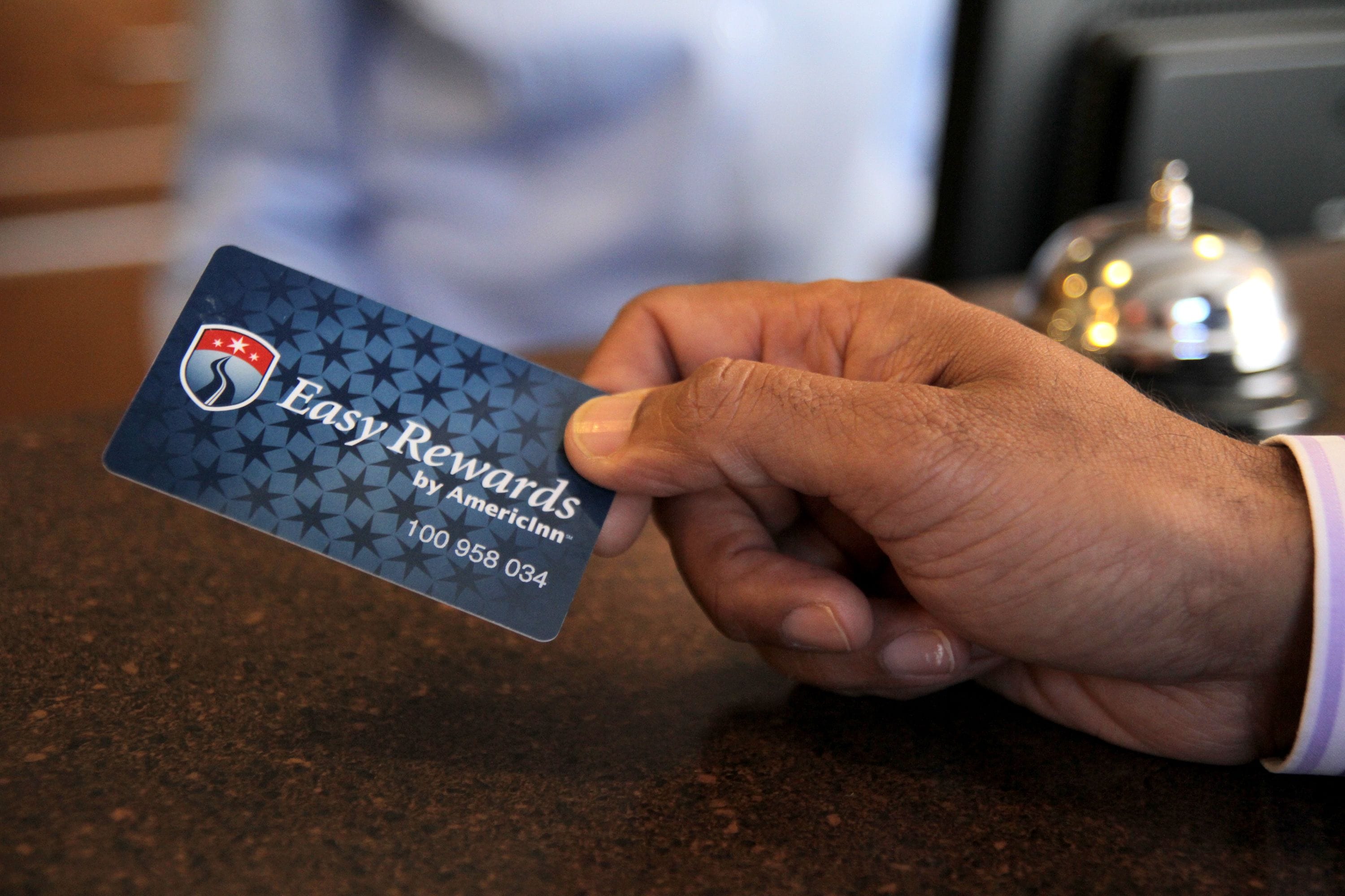 A hand holding a business card with the text "Easy Rewards by AmericInn" and a phone number.