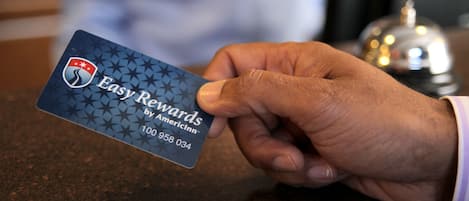 Eine Hand hält eine Visitenkarte mit dem Schriftzug 'Easy Rewards by AmericInn' und einer Telefonnummer.