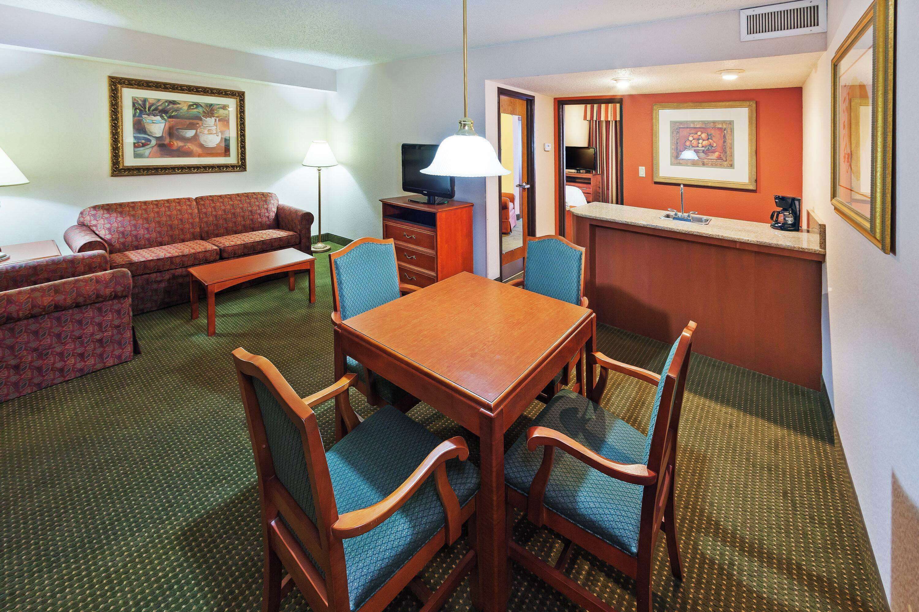 A hotel room with a dining area, a sofa, a TV, and a coffee maker.