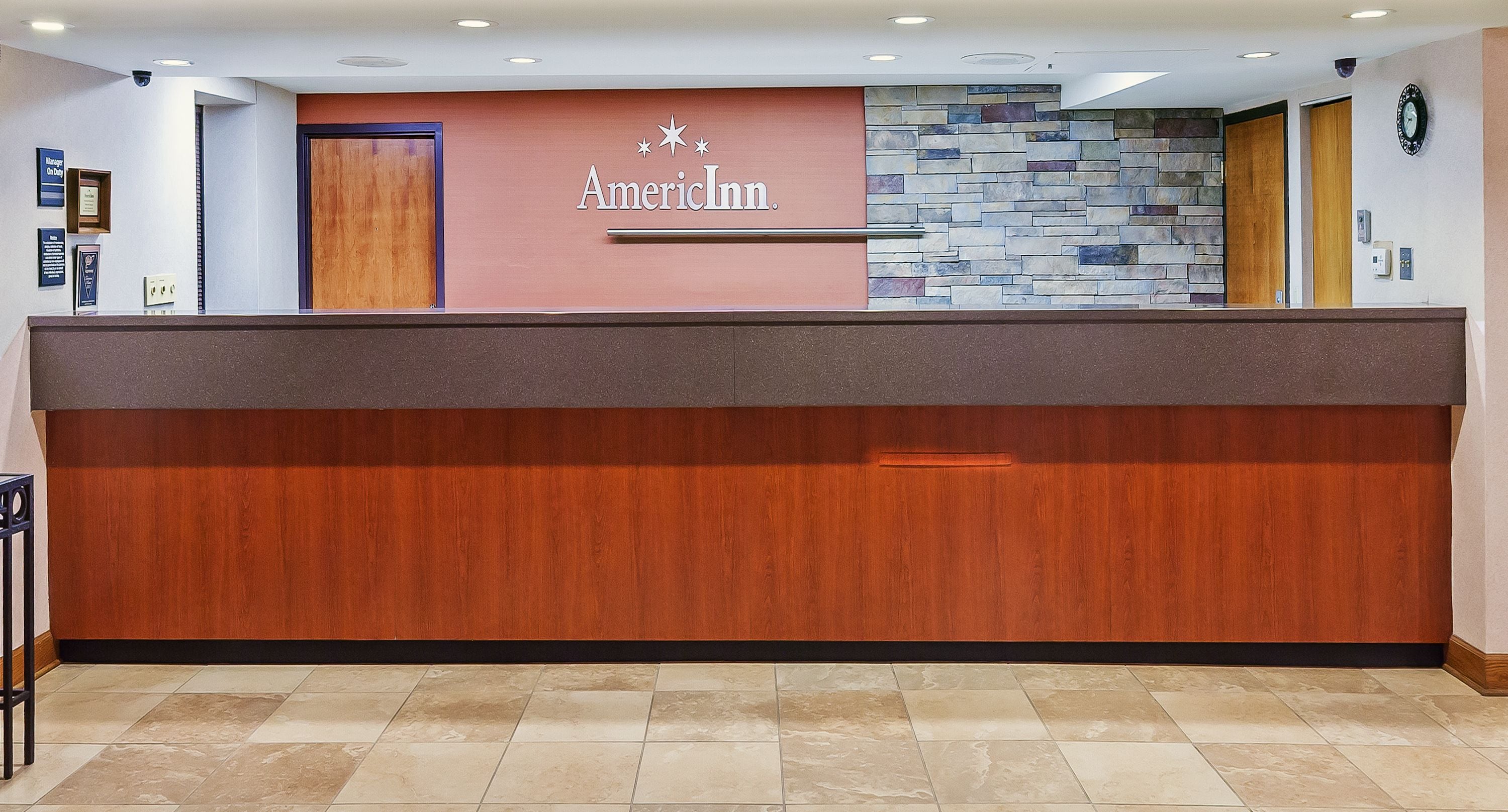 A reception desk with a stone wall and a wooden panel, and a clock on the wall.