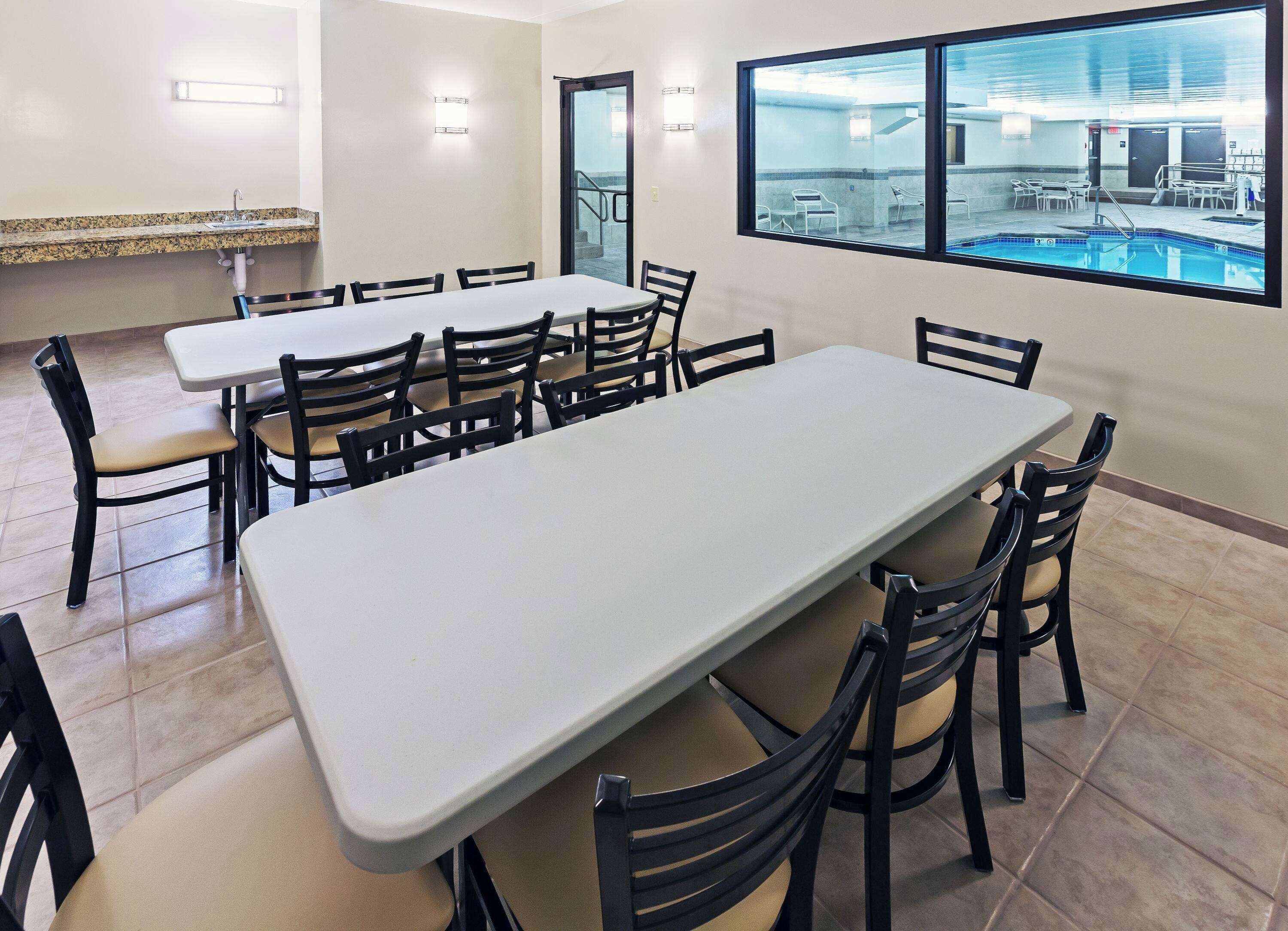 Une salle de conférence équipée de deux longues tables, de chaises noires, d’une fenêtre donnant sur une piscine et d’un petit coin lavabo.