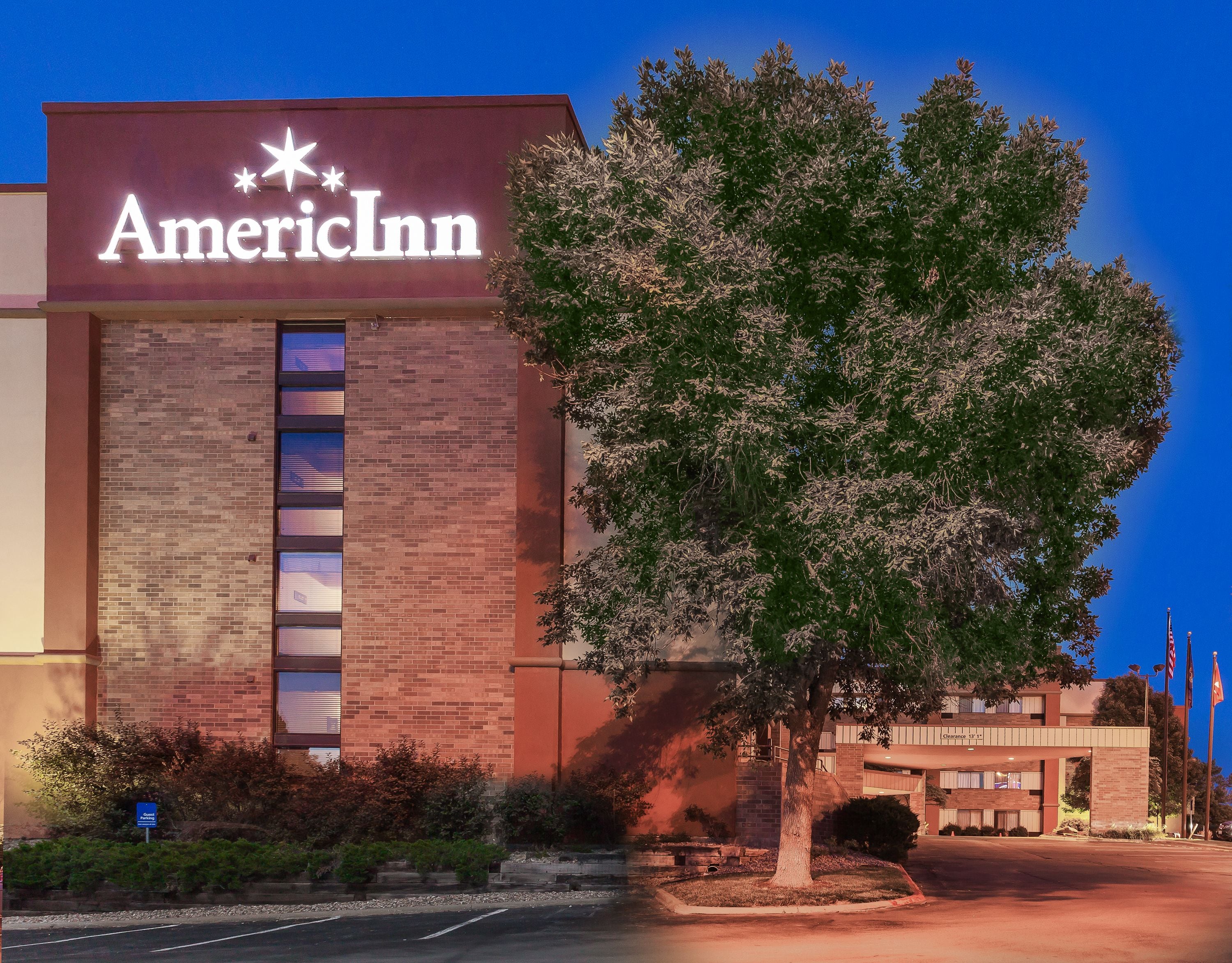 Edificio de American Inn con un letrero llamativo, un árbol grande en el frente y un cielo azul despejado.