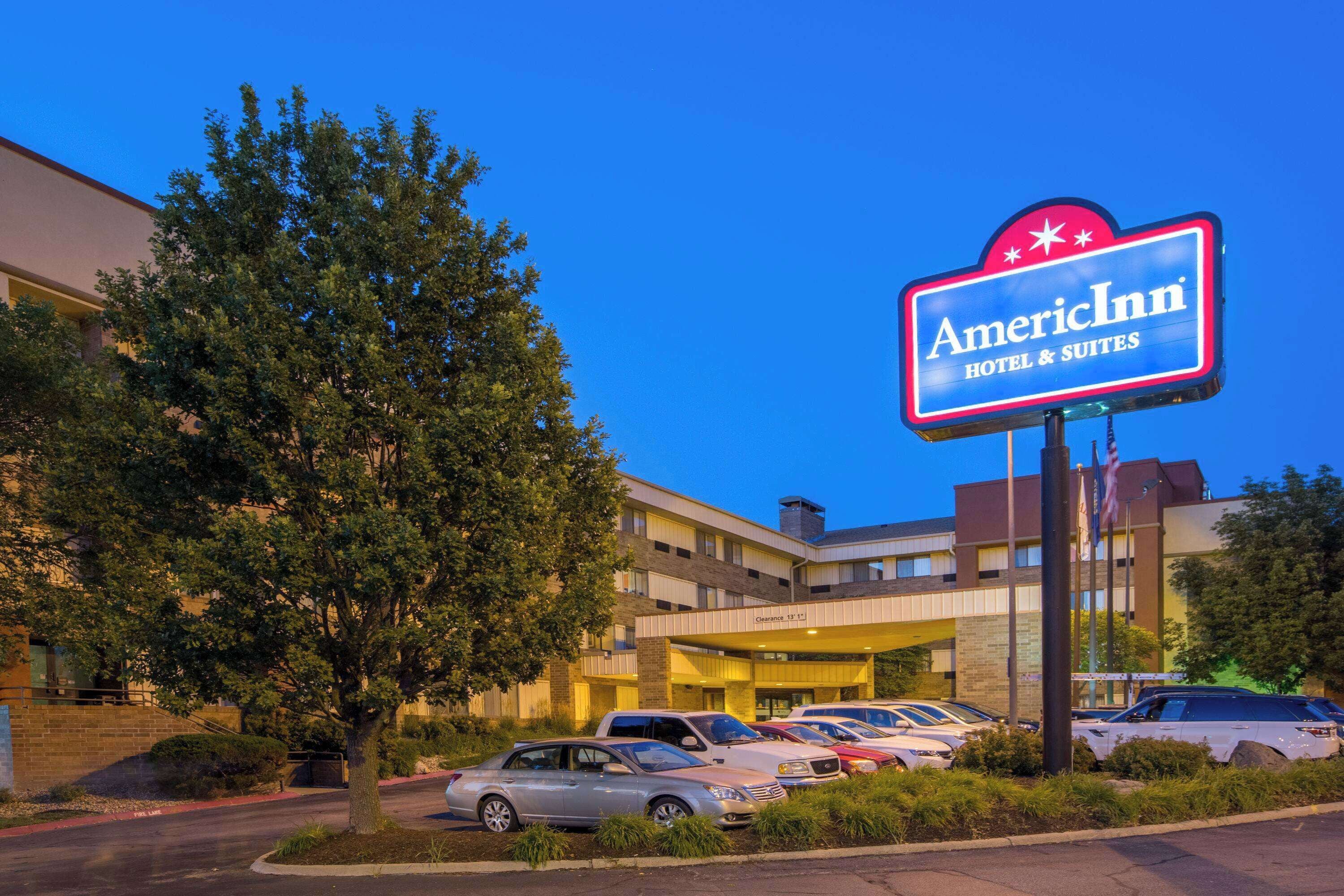 A hotel with a prominent American Inn sign, multiple parking spaces, and a large tree in the foreground.
