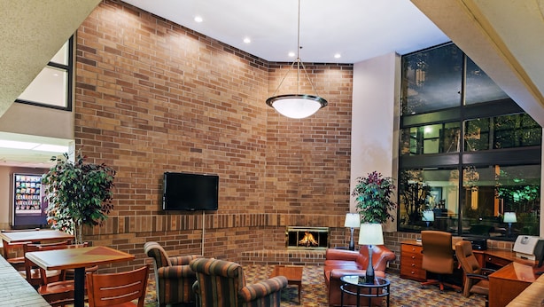 A lobby with a brick wall, a fireplace, seating area, and a television. - AmericInn by Wyndham Omaha (Omaha)