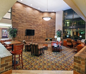 A lobby with a brick wall, a fireplace, seating area, and a television. - AmericInn by Wyndham Omaha (Omaha)