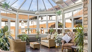 A sunroom with wicker furniture, potted plants, and a view of the city. - Dragonfly Hotel Bury St Edmunds (Bury St Edmunds)