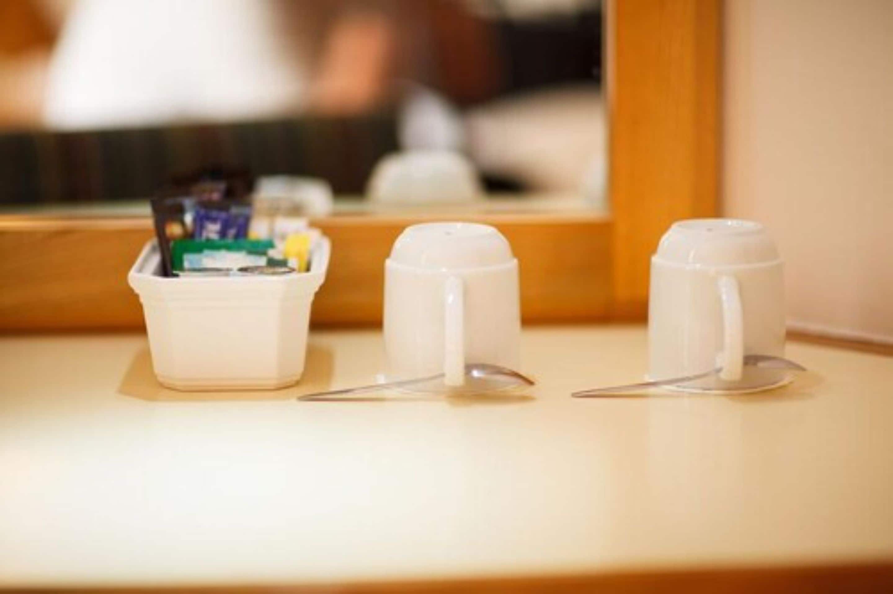 A countertop with a small container holding toiletries and two white mugs with lids.