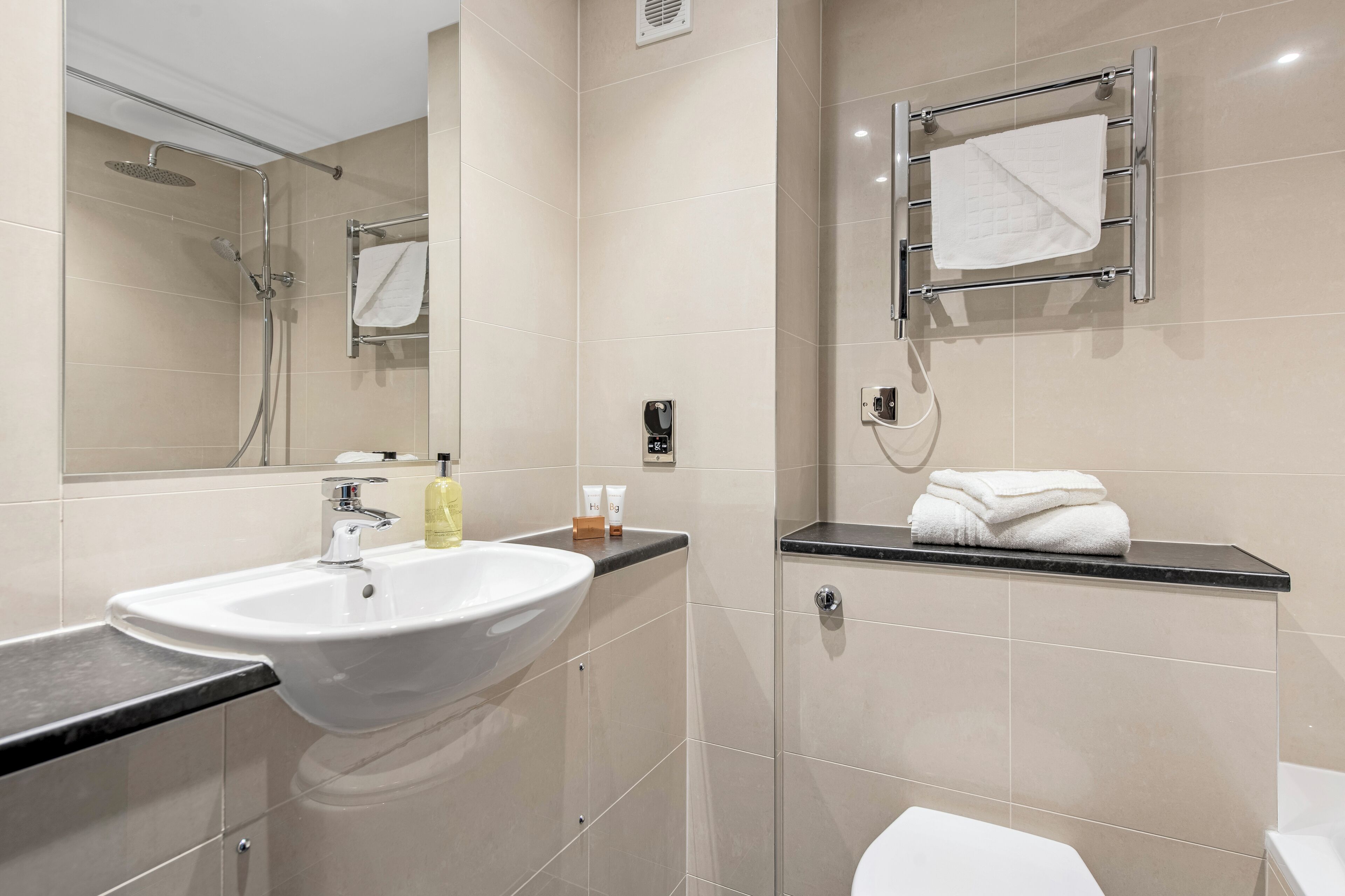 Un baño moderno con un lavamanos grande, ducha e inodoro. Hay toallas y artículos de aseo en la encimera.