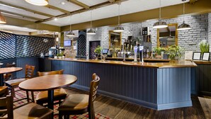 A bar area with wooden tables and chairs, a reception desk, and a stone wall backdrop. - Dragonfly Hotel Bury St Edmunds (Bury St Edmunds)
