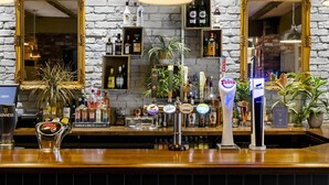 A bar area with a wooden counter, multiple taps including Guinness and Carling, shelves with bottles, and two large mirrors. - Dragonfly Hotel Bury St Edmunds (Bury St Edmunds)