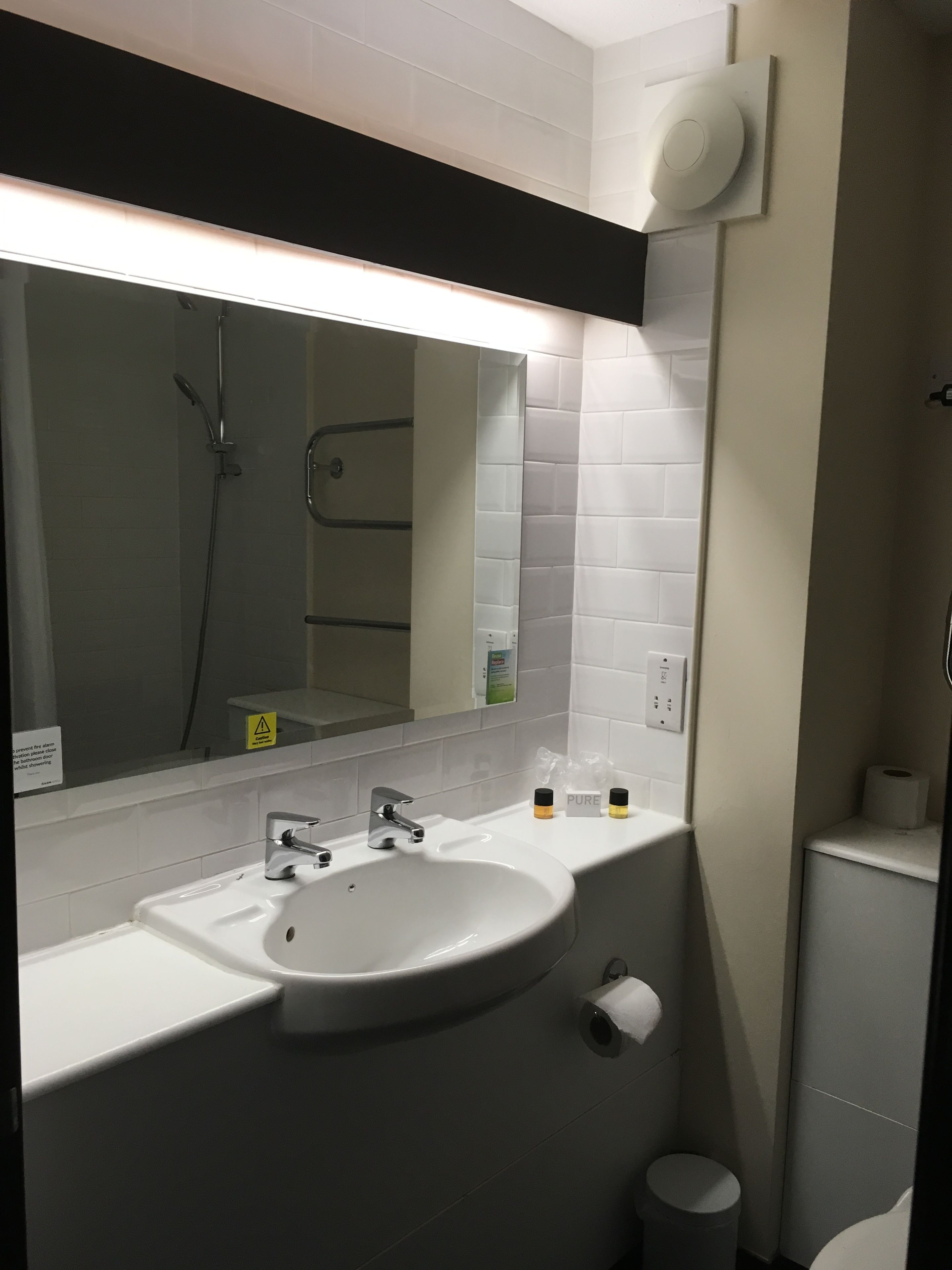 A bathroom with a white sink, mirror, and shower. There are toiletries on the counter.