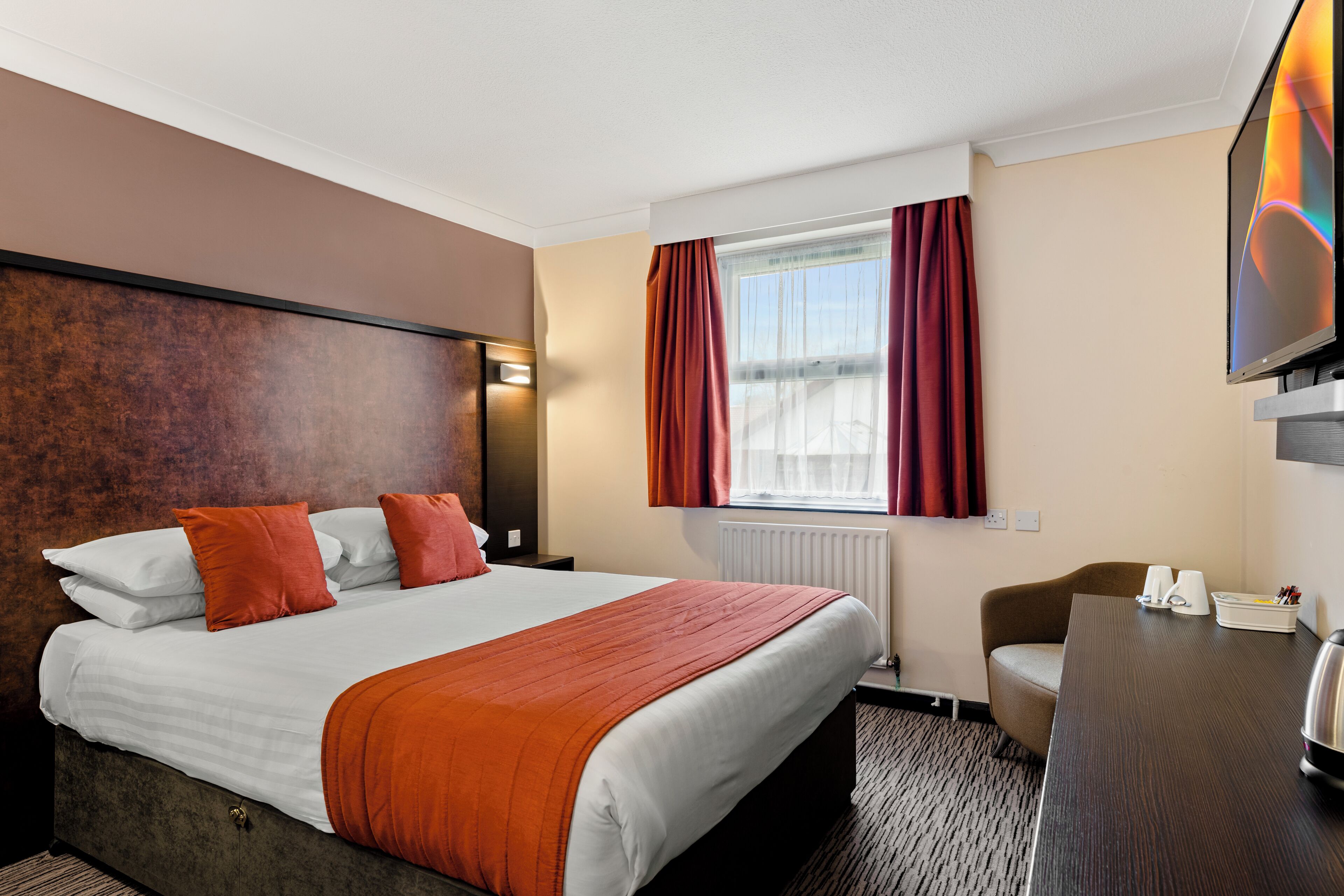 A hotel room with a bed, a desk, a television, and a window with curtains.