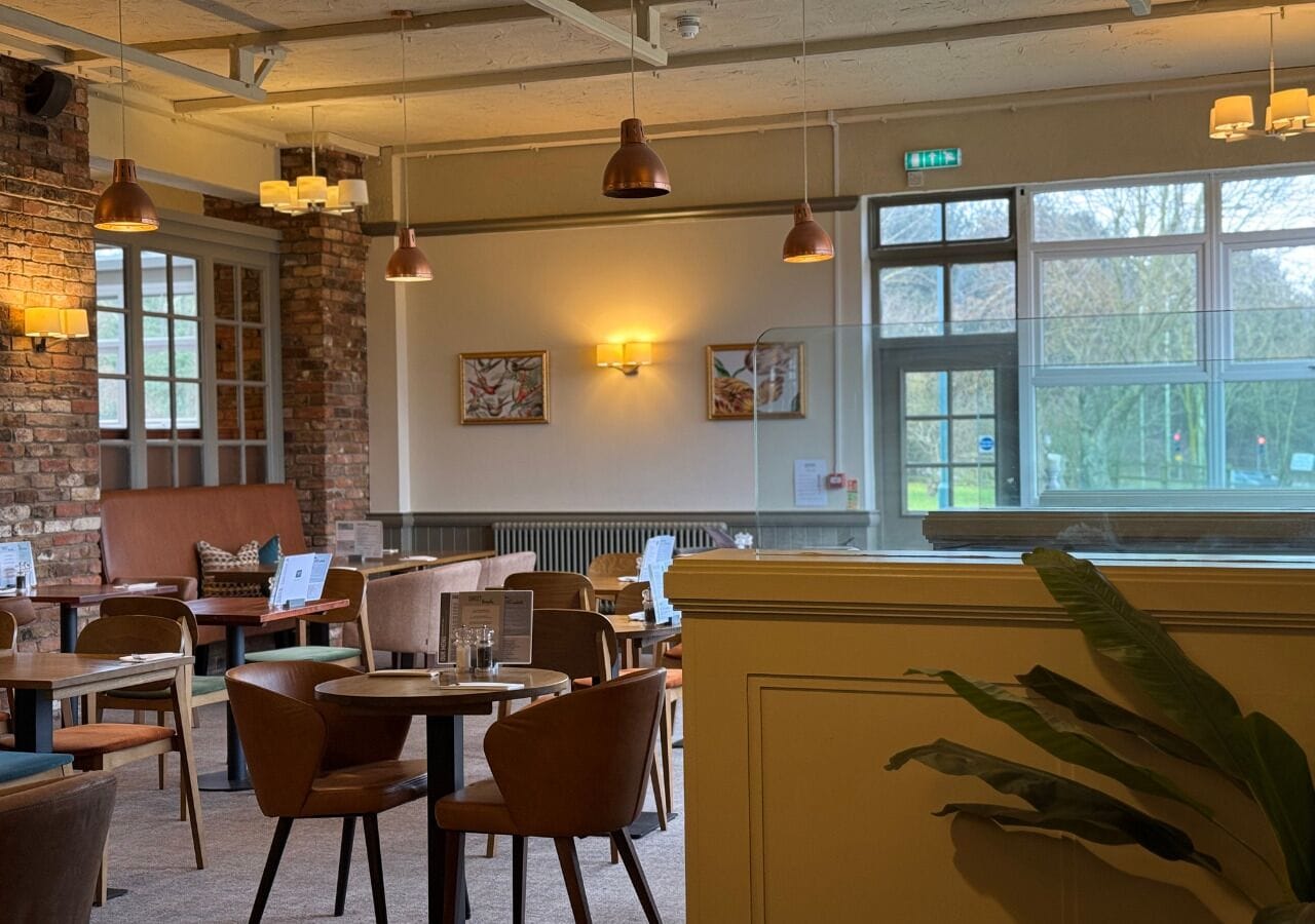 A restaurant with brick walls, wooden tables, and chairs. There are pendant lights and a large window with a view.