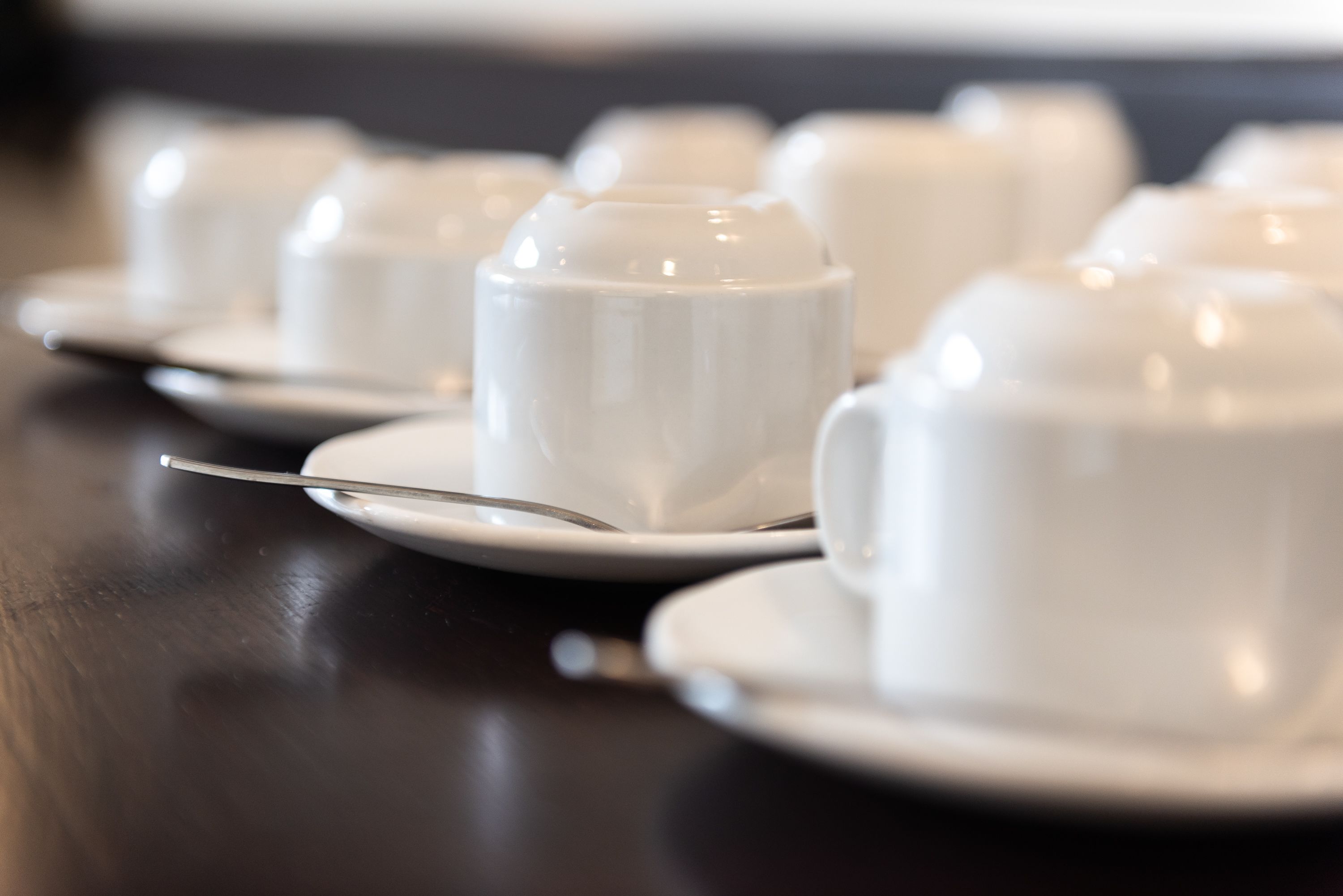 A row of white ceramic cups and saucers on a dark wooden table.