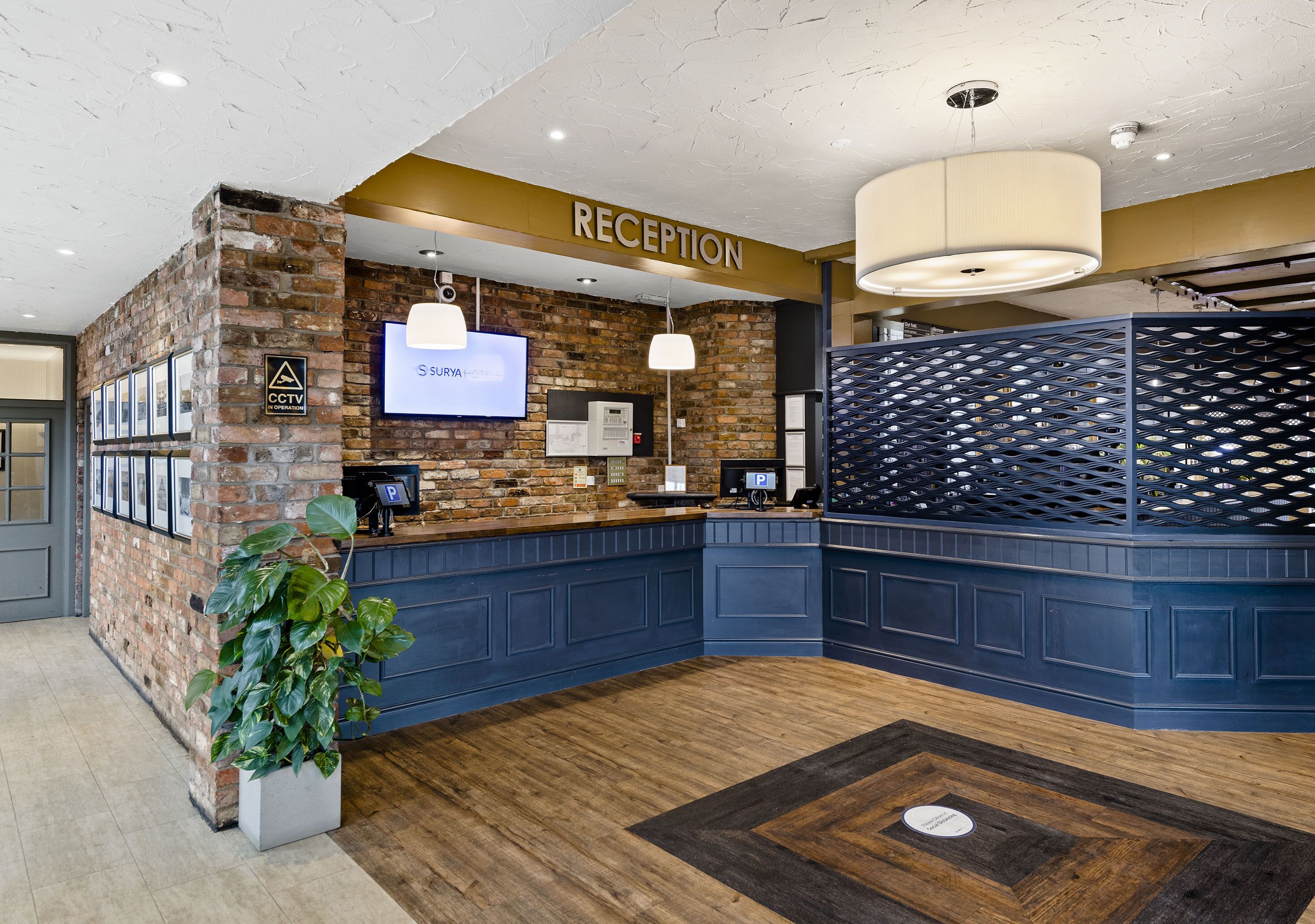 A reception area with a brick wall, a reception desk, a large screen, and a potted plant.
