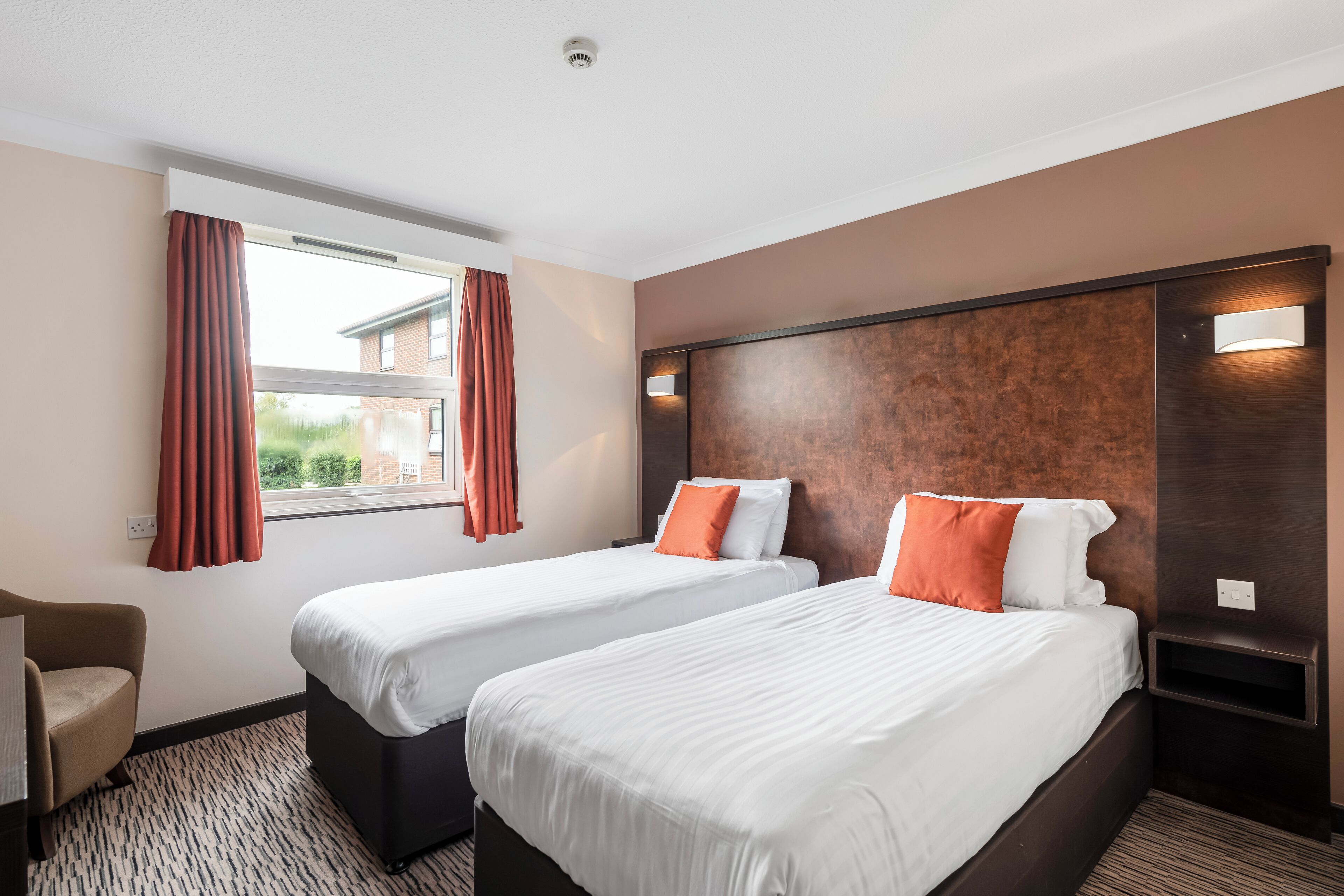A hotel room with two beds, a desk, and a window with curtains.