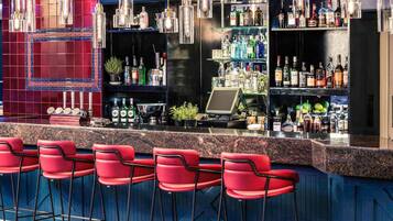 Un área de bar con sillas rojas, una barra con caja registradora y estantes llenos de botellas.