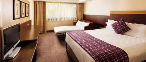 A hotel room with a bed, a sofa, a TV, and a window with curtains.